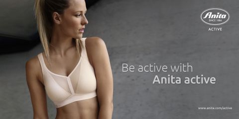 Une femme en soutien-gorge de sport se tient devant un fond gris et regarde sur le côté. Le texte est « Soyez active avec Anita Active. » Le logo Anita et le lien vers le site web se trouvent dans le coin.
