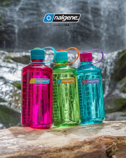 Trois bouteilles d'eau Nalgene colorées (rose, verte et bleue) sont posées sur un tronc d'arbre devant une cascade. Chaque bouteille a un bouchon à vis et une boucle de transport. Le logo Nalgene avec la mention "Fabriqué aux États-Unis" est bien visible.