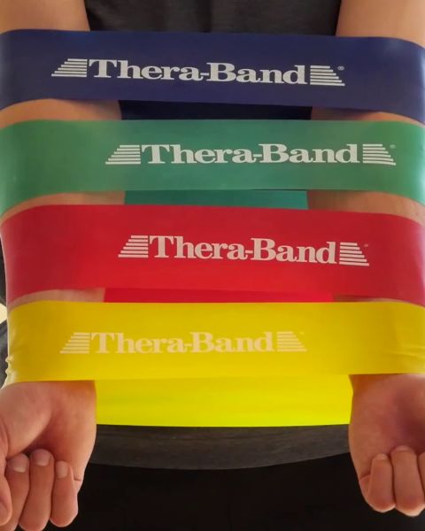 Au premier plan, des bandes de résistance colorées sont suspendues, à l'arrière-plan, un logo Theraband est visible sur le mur. Sur une étagère en dessous se trouvent des équipements d'entraînement et deux bouteilles d'eau.