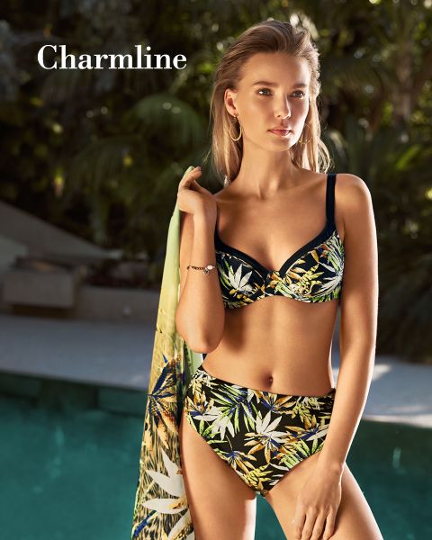 Une personne en bikini à motif tropical se tient au bord d'une piscine et tient un vêtement assorti à la main. La lumière du soleil filtre à travers les arbres environnants et projette des ombres. Dans le coin supérieur gauche, on peut lire le mot « Charmline ».