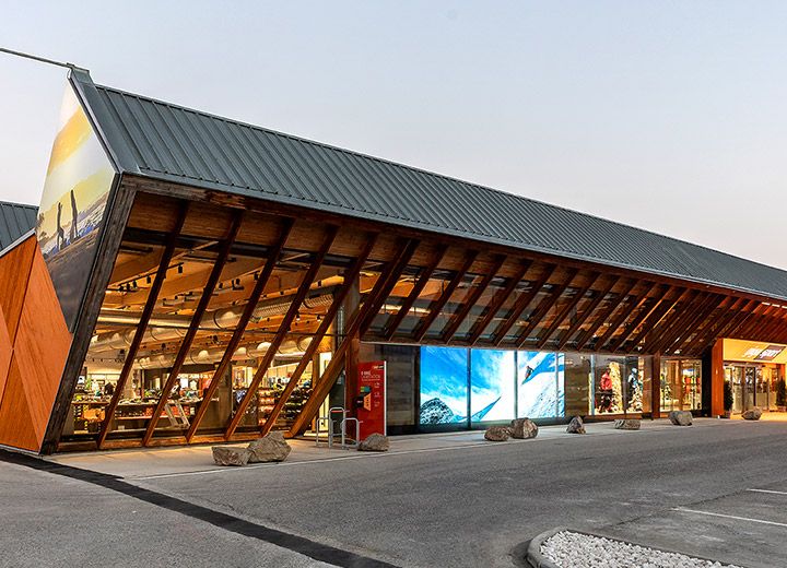 Un bâtiment moderne avec une conception de toit en pente unique, de grandes fenêtres en verre et des éléments en bois, sur fond de ciel clair. Un panneau « German Design Award Winner 2020 » est visible dans le coin supérieur droit. L'extérieur est chaleureusement éclairé.