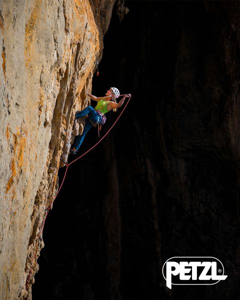 Un grimpeur en veste verte et casque escalade une formation de glace massive et suspendue à l'aide de piolets. Des rochers enneigés entourent la zone. En haut, on peut lire les mots « Experience the Difference » et le logo Petzl.