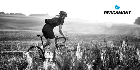 Un cycliste portant un casque roule à vélo de course à travers une prairie, avec un paysage vallonné en arrière-plan. L'image est en noir et blanc et le logo Bergamont est visible dans le coin supérieur droit.