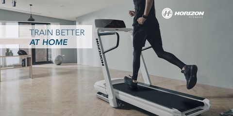 Personne courant sur un tapis de course Horizon Fitness dans une pièce moderne et spacieuse avec parquet et grandes fenêtres. À côté du logo Horizon Fitness, on peut lire : « Entraînez-vous mieux à la maison ».