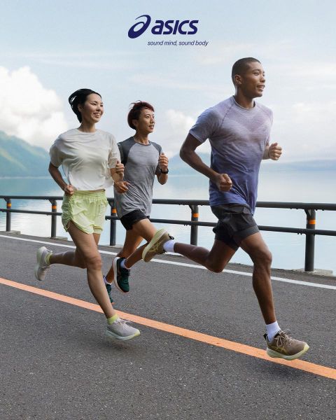 Trois personnes courent sur une route à côté d'une grande étendue d'eau avec des montagnes en arrière-plan. Le ciel est partiellement nuageux. Elles portent des vêtements de sport et semblent concentrées. Le logo ASICS et le slogan figurent en haut de l'image.