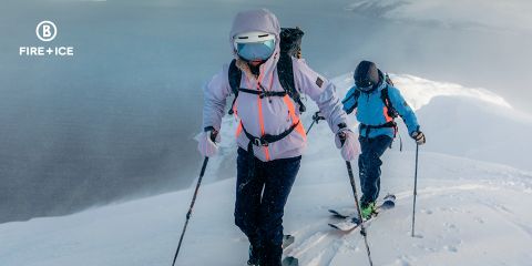 Deux personnes en vêtements d'hiver font du ski en montant une montagne à travers la neige. Ils portent des sacs à dos et utilisent des bâtons pour s'aider. En arrière-plan, on aperçoit un paysage brumeux et vaste. L'image contient un logo « Fire + Ice » dans le coin supérieur gauche.