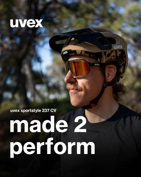 Une personne avec une moustache porte des lunettes UVEX Sportstyle et un casque à l'extérieur. Le texte est : « UVEX sportstyle 237 CV made 2 perform ». On aperçoit des arbres et de la verdure floue en arrière-plan.