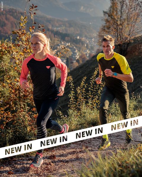 Deux personnes en tenue de sport courent sur un sentier rocailleux à travers un paysage vallonné et boisé. La lumière du soleil met en valeur le feuillage d'automne. Des bannières blanches avec l'inscription "NOUVEAU" en caractères noirs gras traversent la partie inférieure de l'image.