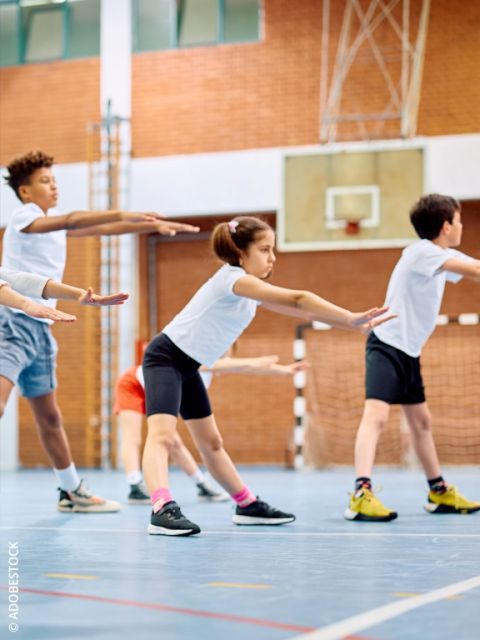 Gros plan sur un enfant portant des baskets grises avec des swooshes Nike rouges, debout sur une surface bleue. L'arrière-plan est flou avec des formes douces et colorées.