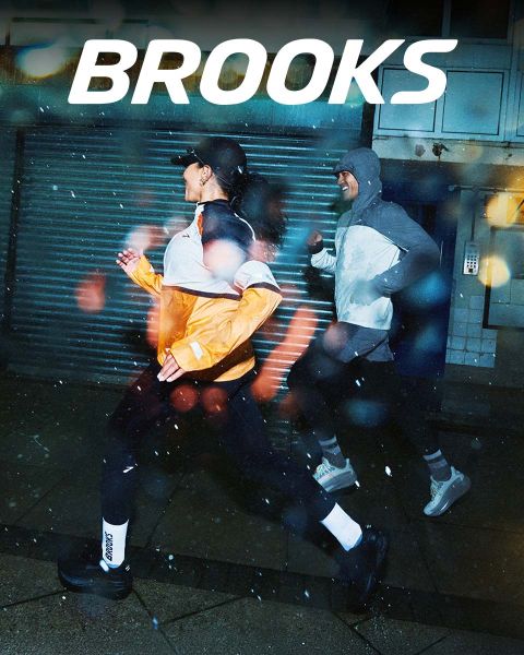 Un groupe de cinq personnes traverse énergiquement un passage piéton. Ils portent des vêtements de sport colorés, notamment des shorts et des débardeurs. La scène est animée, et le mot « BROOKS » est bien visible au-dessus d'eux.