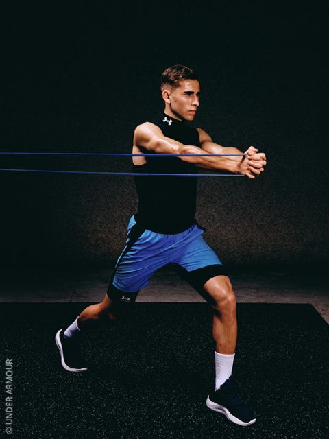 Un homme en tenue de sport effectue un exercice avec une bande de résistance, debout en position de fente, étirant les bandes avec les deux bras tendus vers l'avant devant un fond sombre.
