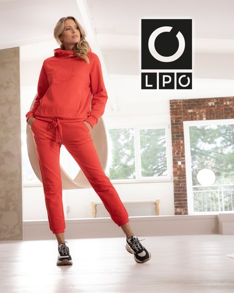 Un homme en t-shirt bleu et pantalon foncé fait un exercice de corde ondulatoire dans une salle de sport de style industriel avec deux grandes fenêtres cintrées en arrière-plan. La lumière entre et les lettres « LPO » apparaissent dans le coin supérieur droit.