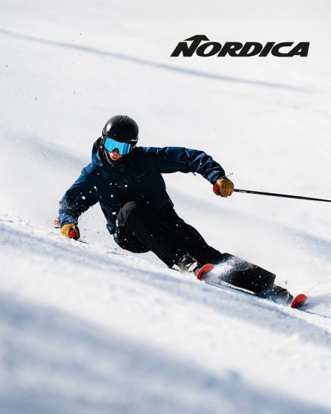 Deux skieurs en équipement de protection - l'un en bleu, l'autre en foncé - dévalent une pente enneigée. Le logo « Nordica » est visible en haut. Tous deux sont inclinés, démontrant rapidité et agilité par une journée ensoleillée.