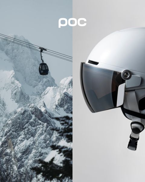 Une personne portant un manteau d'hiver orange et un casque se tient au sommet d'une montagne enneigée et regarde les montagnes enneigées au loin. Le logo POC est visible sur le casque et dans le coin supérieur droit de l'image.