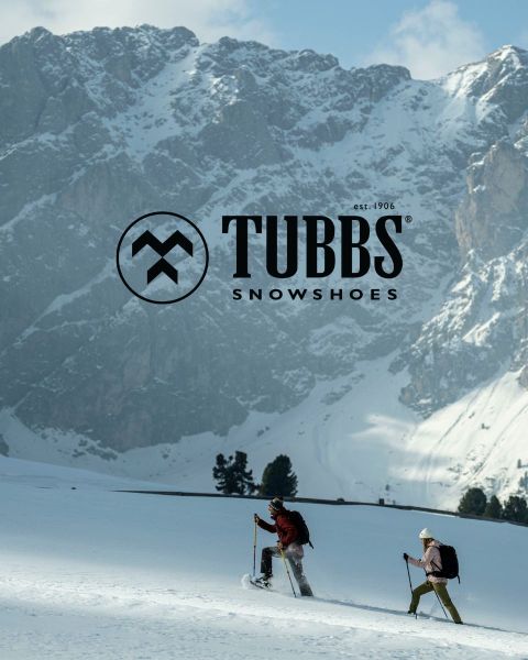 Deux personnes montant une pente enneigée avec des bâtons de ski, avec en arrière-plan de hautes montagnes escarpées et enneigées. Le logo Tubbs Snowshoes apparaît au-dessus de l'image.