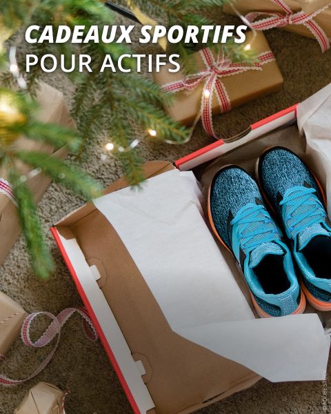 Une paire de chaussures de course bleues dans une boîte ouverte se trouve sous un arbre de Noël, entourée de cadeaux emballés. Cadeaux sportifs pour actifs.