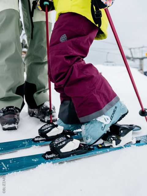 Deux personnes en vêtements de ski colorés se tiennent dans la neige avec des skis et des bâtons, prêtes à skier. Seules leurs jambes et leurs skis sont visibles.