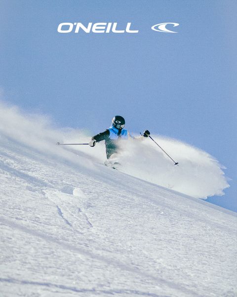 Une femme aux cheveux longs se tient dans un paysage désertique sous un ciel bleu avec quelques nuages épars. Elle porte un débardeur noir O'Neill et se penche légèrement en avant. Le logo O'Neill est visible sur le côté droit de l'image.