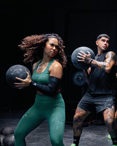 Deux personnes en tenue de sport tiennent des ballons médicinaux pendant qu'elles s'entraînent dans une salle de sport. Les deux ont l'air concentrées et actives.