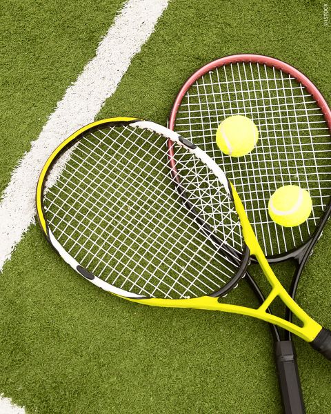 Deux raquettes de tennis et deux balles de tennis sont posées sur un terrain vert avec une ligne blanche en arrière-plan.
