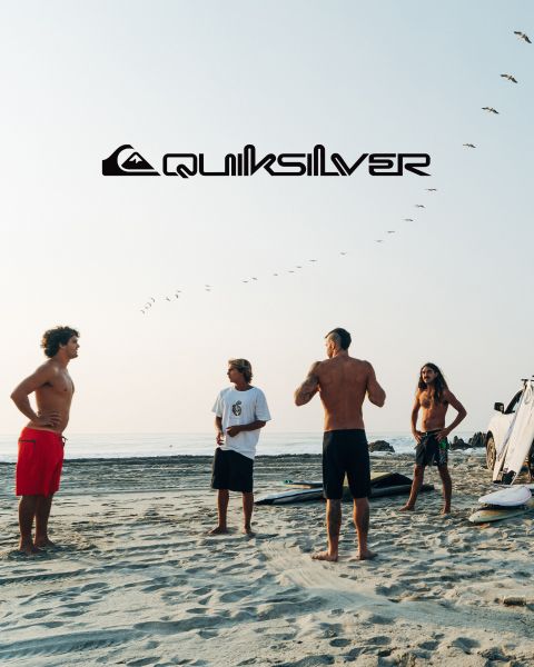 Un surfeur chevauche une grande vague turquoise, incarnant l'équilibre et l'habileté. Il porte un short de bain foncé, et la vague se brise au-dessus de lui. Au-dessus de lui, on peut voir le logo Quiksilver.