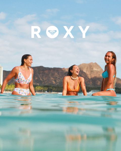 Trois femmes nagent en maillot de bain sous l'eau claire et bleue. L'une porte un haut à manches longues, les autres des bikinis. L'image est superposée avec le logo blanc "Roxy".