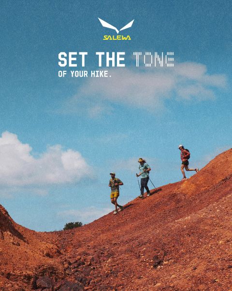 Une personne en veste blanche et lunettes de soleil escalade un terrain rocheux. L'effet de flou de mouvement accentue la vitesse et le mouvement. En haut, on peut lire le texte « MXT Forward A Fast Story », et à droite le logo Salewa.