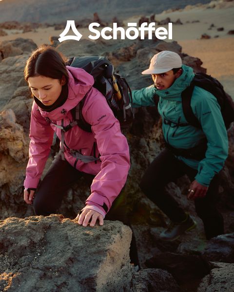 Deux personnes en équipement de plein air marchent sur une colline herbeuse avec des montagnes et des nuages en arrière-plan. Au-dessus d'eux se trouve le logo Schöffel, en dessous une ligne ondulée verte décorative.