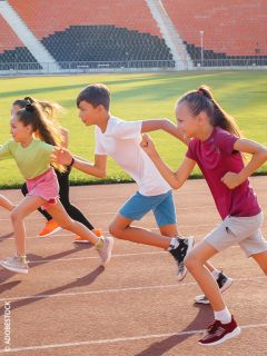 Quatre enfants sprintent sur une piste d'athlétisme dans un stade, sourient et profitent de la course par une journée ensoleillée.
