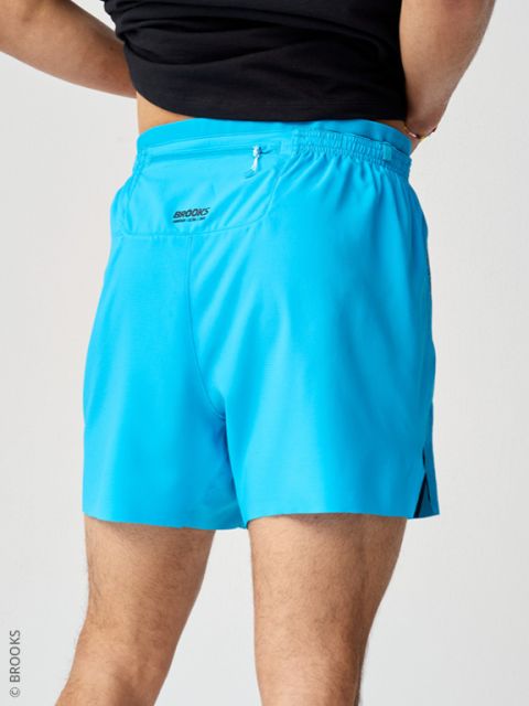 Personne en pantalon de survêtement bleu clair et haut noir, photographiée de dos devant un fond clair.