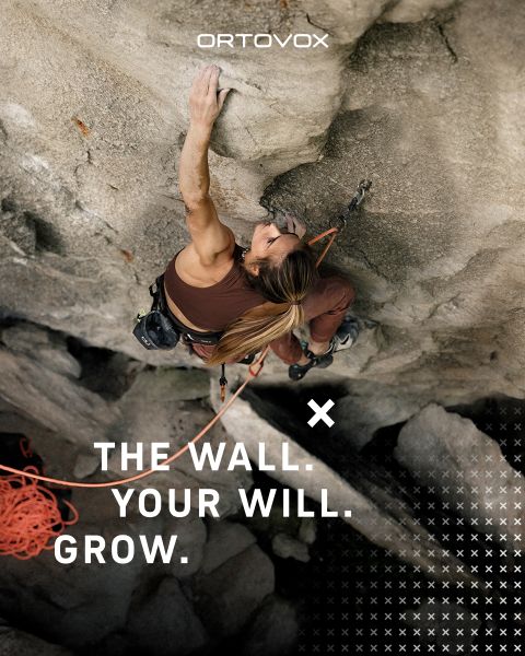 Trois personnes en équipement de plein air sont assises, souriantes et discutant sur un terrain rocheux dans une région montagneuse. Le soleil se couche derrière les sommets. Un sac à dos et une thermos sont posés à proximité. Le logo d'Ortovox se trouve en haut à droite.