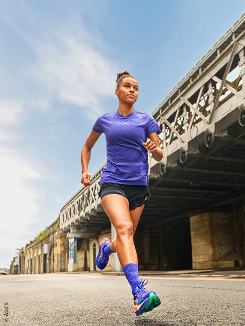 Une femme en tenue de sport court en plein air sur une rue de ville sous un grand pont métallique par une journée claire.
