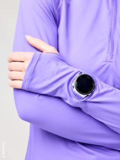 Une personne vêtue d'une chemise à manches longues violette croise les bras et porte une montre intelligente noire ronde par-dessus sa manche.