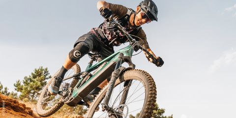 Un cycliste équipé de protections descend un chemin de terre avec son VTT par une journée ensoleillée, se penchant brusquement dans un virage.