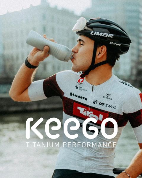 Un cycliste portant un maillot blanc et rouge boit à une bouteille et porte un casque sur lequel le texte « KEEGO Titanium Performance » est affiché.