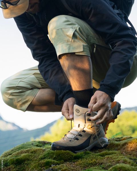 Gros plan de deux randonneurs debout sur un terrain rocheux, regardant leurs chaussures de trail La Sportiva sous un ciel bleu clair.