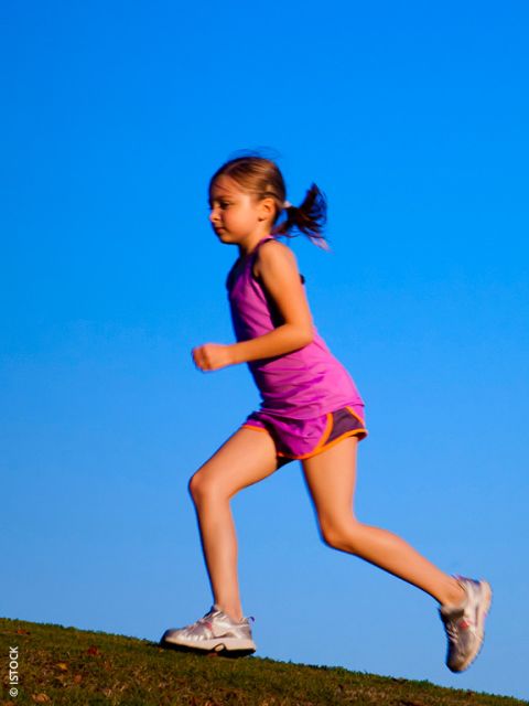 Jeune fille en tenue de sport rose courant en plein air sur une colline avec un ciel bleu clair en arrière-plan.