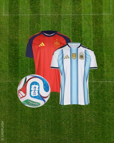 Deux maillots de football - l'un rouge et l'autre blanc à rayures bleues - à côté d'un ballon de football coloré sur un terrain de gazon vert.
