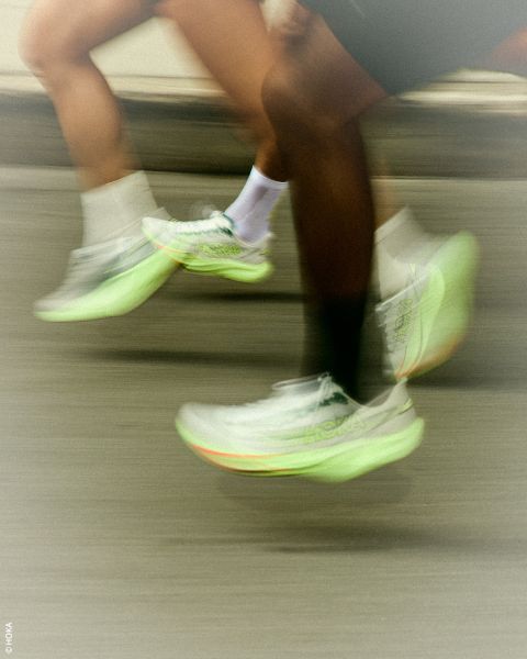 Deux personnes courant avec des baskets HOKA vert néon ; un flou de mouvement souligne leur déplacement rapide sur une route.