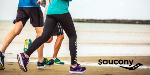 Trois personnes courent en tenue de sport le long d'une plage de sable ; le logo Saucony est visible dans le coin inférieur droit.