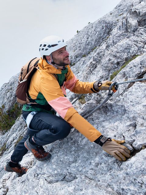 Un homme en équipement d'escalade gravit une paroi rocheuse, se tenant à une corde de sécurité avec un mousqueton.