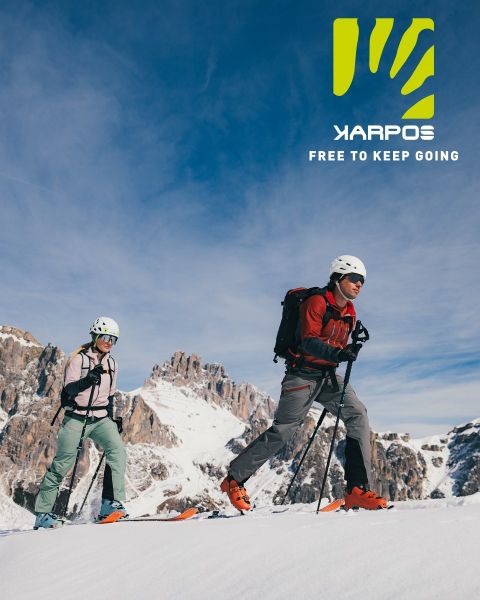 Un cycliste en veste rouge et casque bleu descend un chemin herbeux sur un VTT orange vif. En arrière-plan, on aperçoit des arbres aux couleurs automnales. En haut à droite, on peut lire le texte « KARPOS LIBRE DE CONTINUER ».