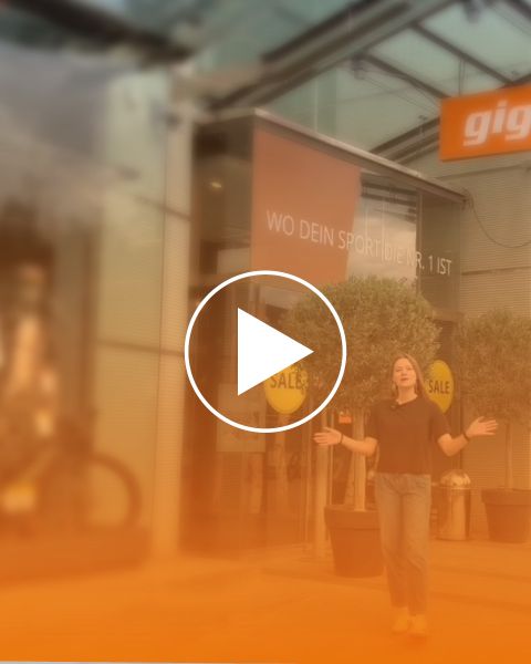 Une femme se tient devant un magasin avec des panneaux « Sale » et une bannière indiquant « OÙ VOTRE SPORT EST LE N°1 ». La scène est baignée d'une lumière orange.
