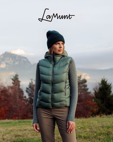 Trois personnes en vêtements d'hiver font du ski dans un paysage montagneux enneigé sous un ciel clair. Le texte est : "LaMunt MOUNTAIN ME-TIME". On aperçoit des sommets enneigés en arrière-plan.