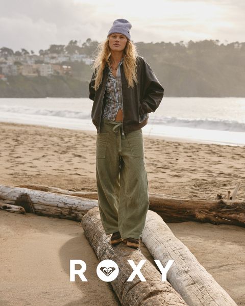Trois femmes nagent en maillot de bain sous l'eau claire et bleue. L'une porte un haut à manches longues, les autres des bikinis. L'image est superposée avec le logo blanc "Roxy".