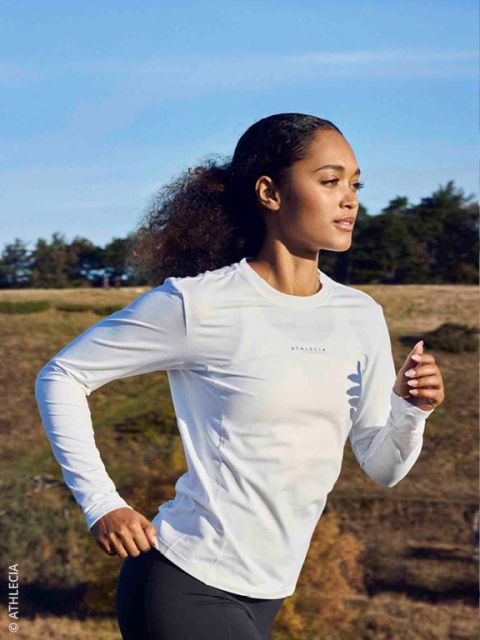 Quatre personnes en tenue de course d'hiver font du jogging ensemble sur un chemin enneigé sous un pont en béton, sourient et profitent de l'exercice en plein air.