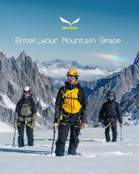Une personne en veste blanche et lunettes de soleil escalade un terrain rocheux. L'effet de flou de mouvement accentue la vitesse et le mouvement. En haut, on peut lire le texte « MXT Forward A Fast Story », et à droite le logo Salewa.