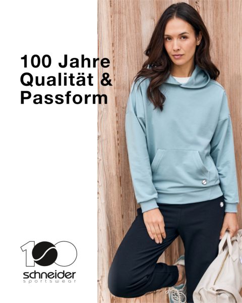 Une personne aux cheveux mi-longs, portant une veste décontractée et un t-shirt, se tient devant un fond neutre. En haut de l'image, on peut lire l'inscription "Schneider Sportswear".