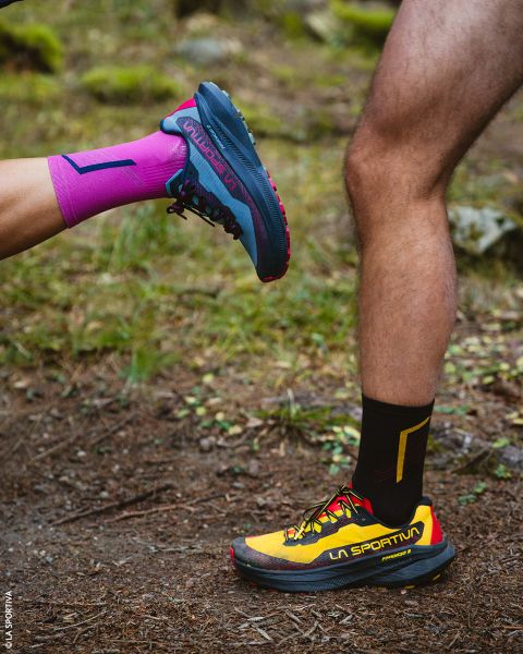 Deux jambes en chaussures de trail et chaussettes de sport, debout sur un chemin de terre.
